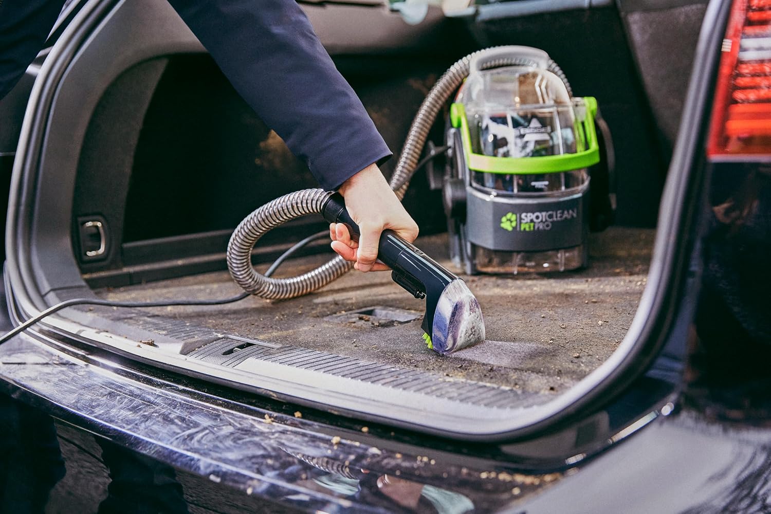 Nettoyage du coffre d’une voiture avec le tuyau du SpotClean Pet Pro, l’appareil posé dans le coffre ouvert